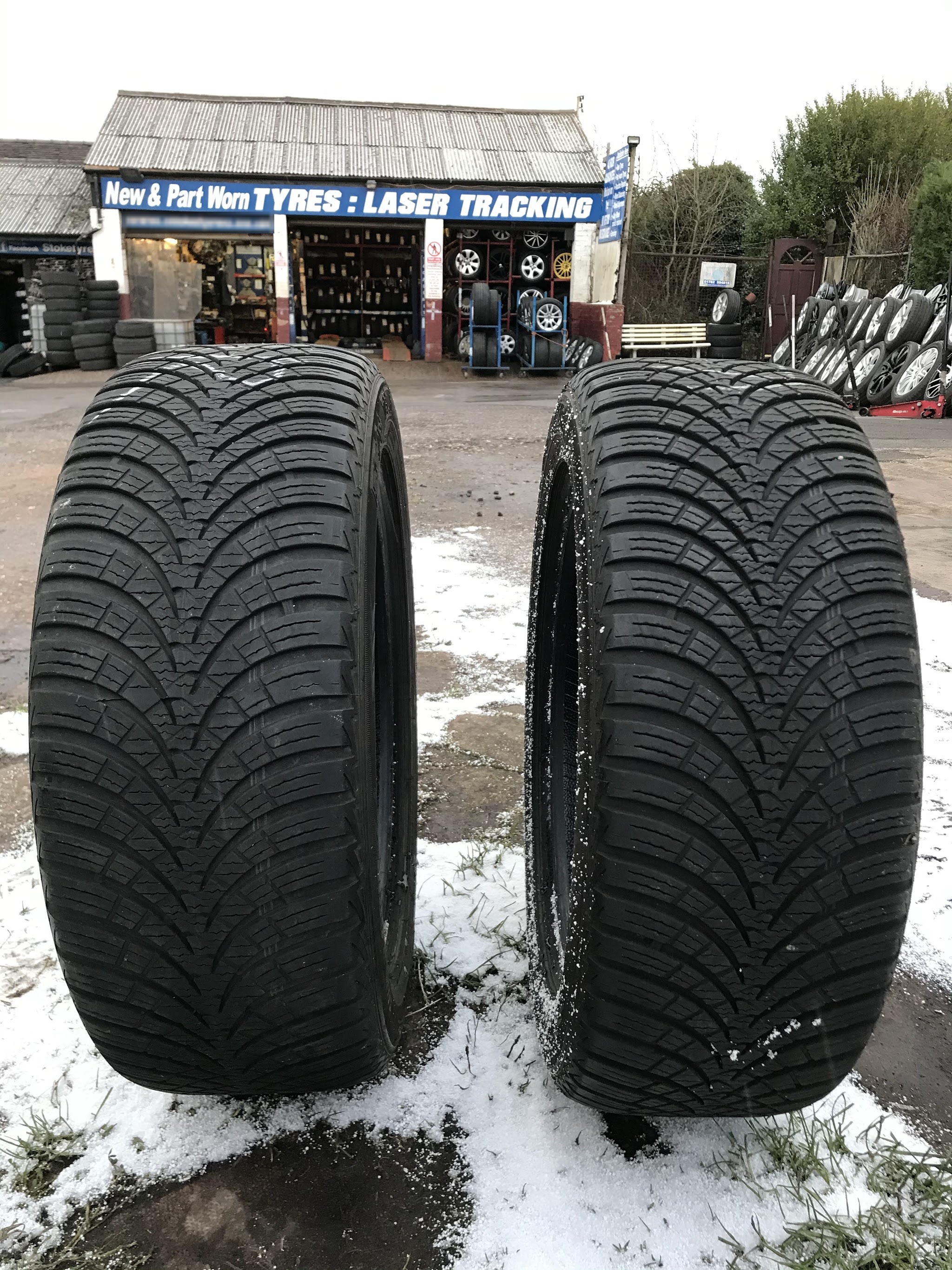 Two tyres standing on the snowy forecourt in front of the New and Part Worn Tyres and Laser Tracking sign